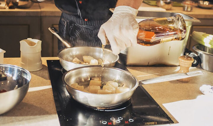 person with vinyl gloves holding oil bottle in front of stove