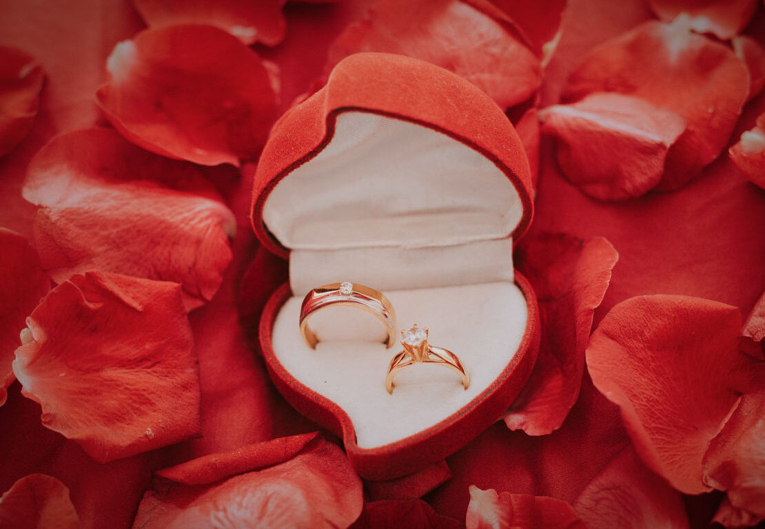 rings inside heart-shaped ring box with red rose petals as the background