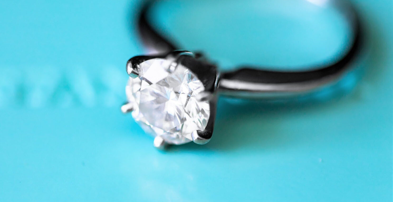 macro shot of a sterling silver solitaire ring against a teal blue background