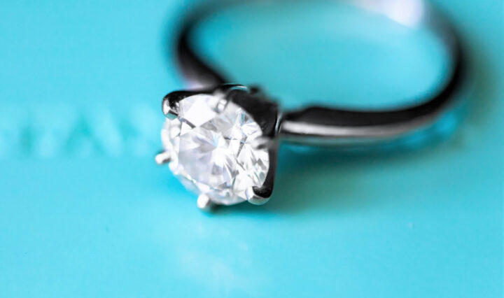 macro shot of a sterling silver solitaire ring against a teal blue background