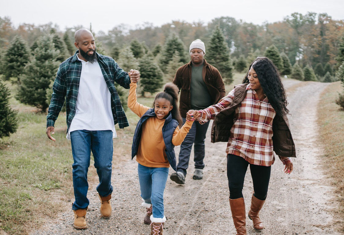 smiling family of four walking on tree farm road