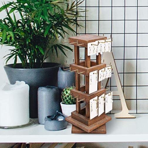 Natural Wood Rotating 36 Hook-Jewelry Display from Nile Corp on top of a white table with a pot of plant